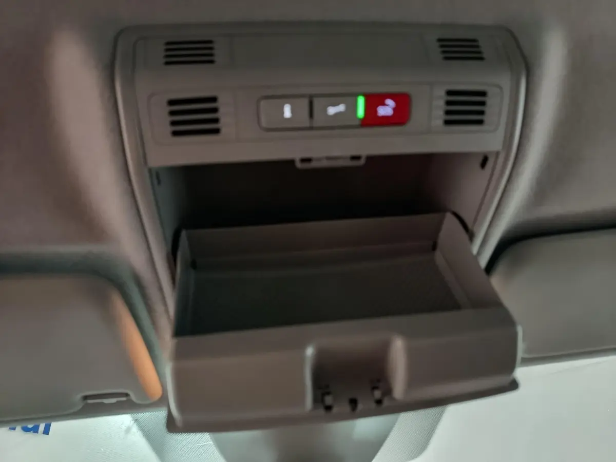 Vue intérieure en plongée du rangement plafond ouvert du Skoda Kamiq gris clair 2024 avec commandes d'urgence et ventilation.