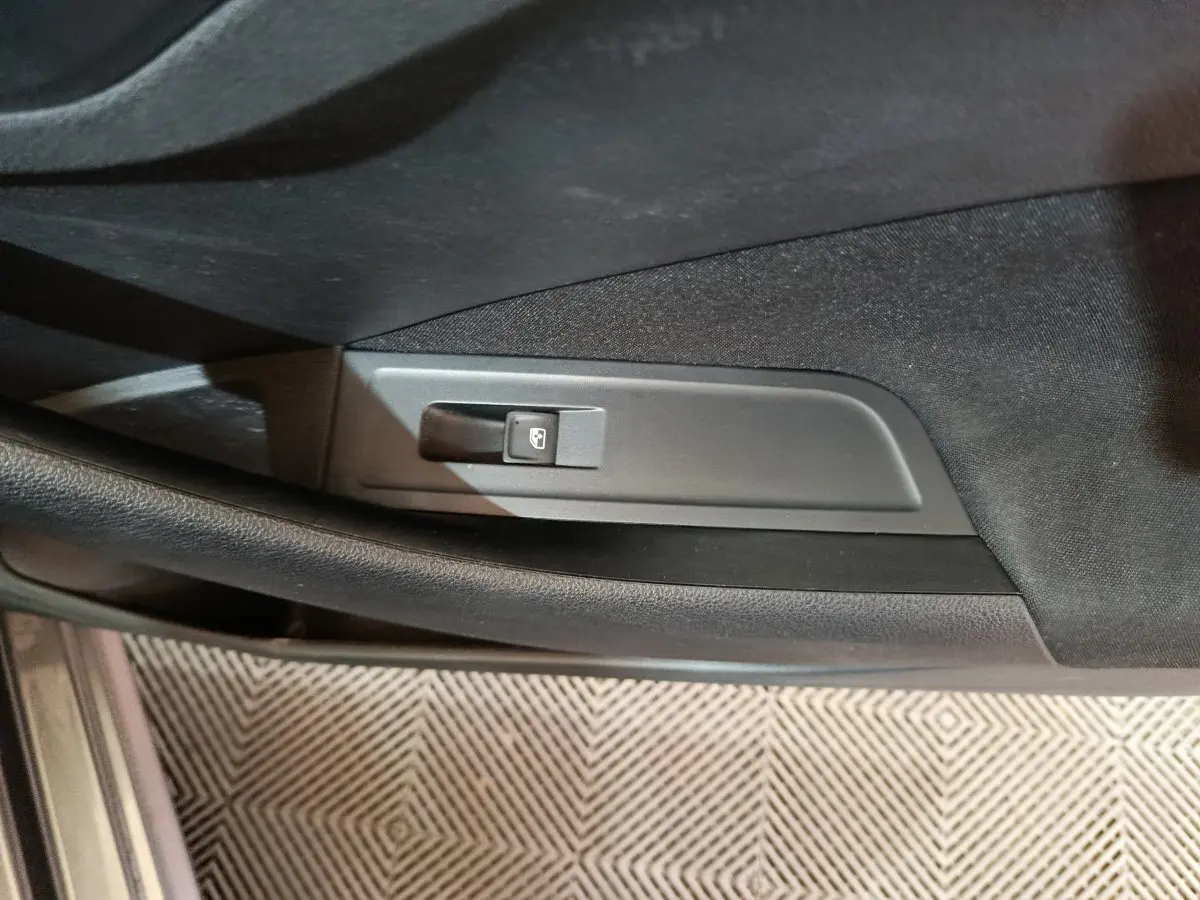 Gros plan sur le bouton de commande de la vitre électrique côté conducteur dans l'habitacle noir du Skoda Kamiq gris clair.
