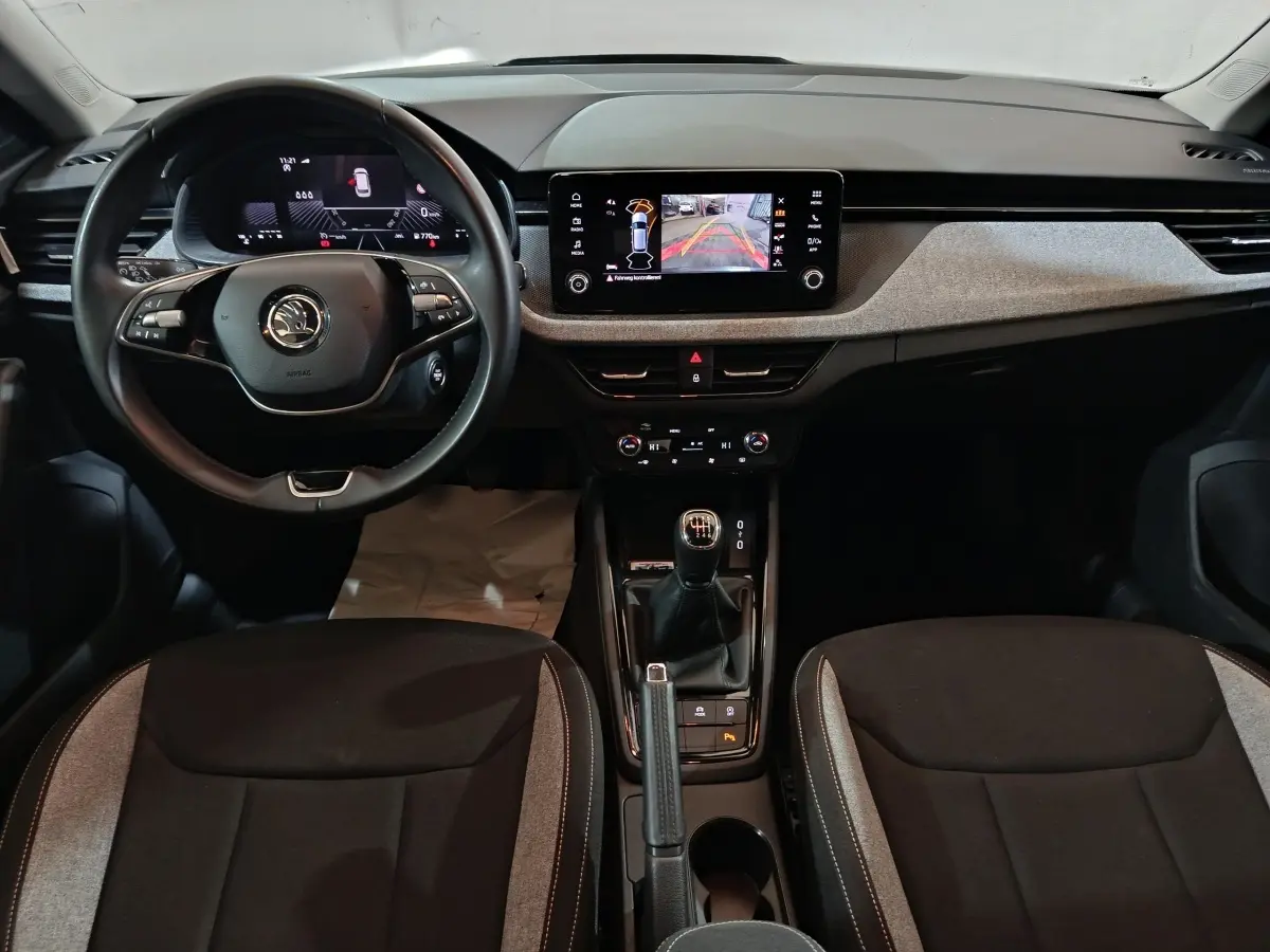 Intérieur de la Skoda Kamiq 2024, vue frontale du poste de conduite avec volant cuir et écran tactile central.