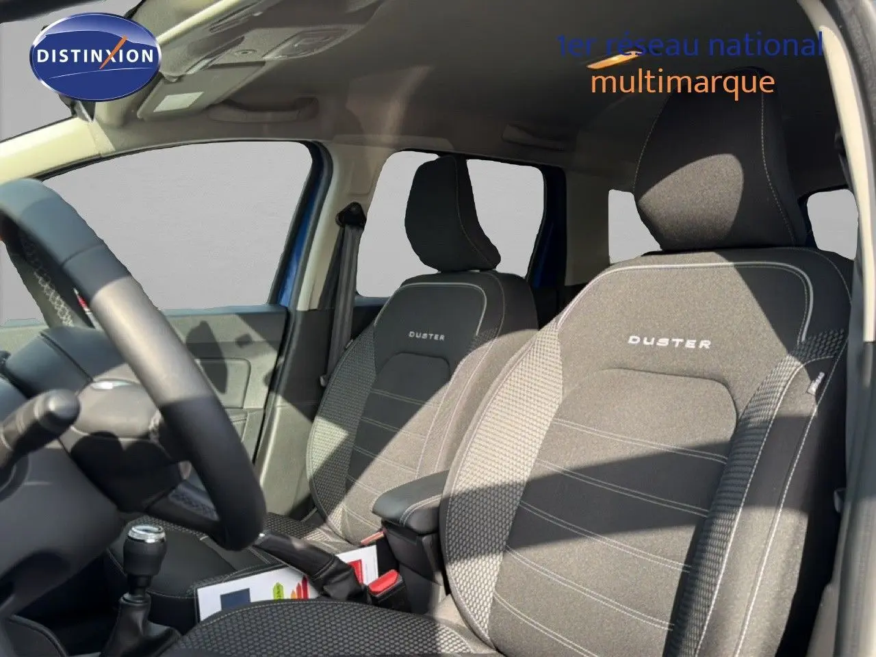 Vue intérieure côté conducteur du Dacia Duster 2022 bleu iron, mettant en valeur les sièges tissu gris avec logo Duster brodé.