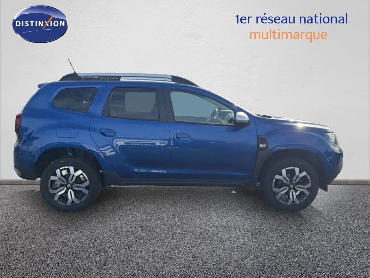 Profil droit d’un Dacia Duster 1.0 ECO-G 100 Prestige bleu Iron 2022 avec jantes bi-ton et barres de toit.