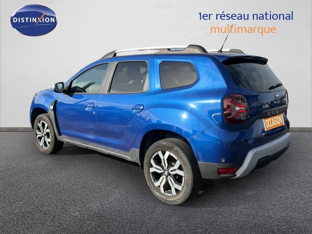 Vue 3/4 arrière droite d'un Dacia Duster bleu Iron 2022 avec jantes alliage et toit noir contrasté.