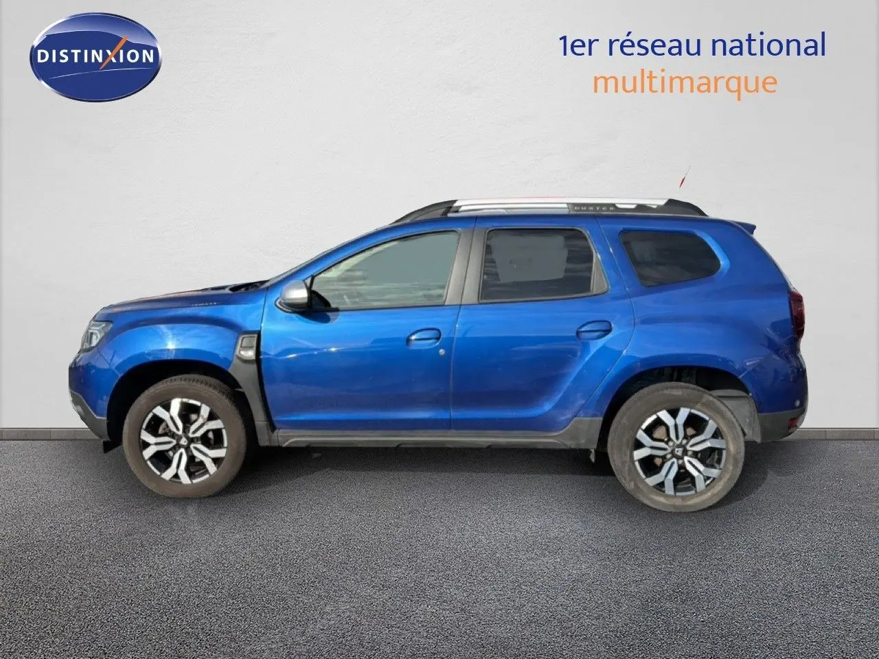 Vue latérale gauche d’un Dacia Duster 2022 bleu Iron avec jantes alliage bicolores et barres de toit.