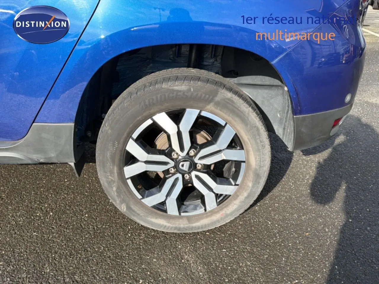 Gros plan sur la roue arrière droite du Dacia Duster bleu Iron 2022 avec jante alliage bicolore.