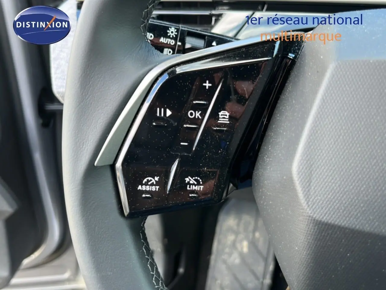Gros plan sur les commandes noires du volant en cuir gris du Peugeot 5008 2025 hybride, côté gauche.