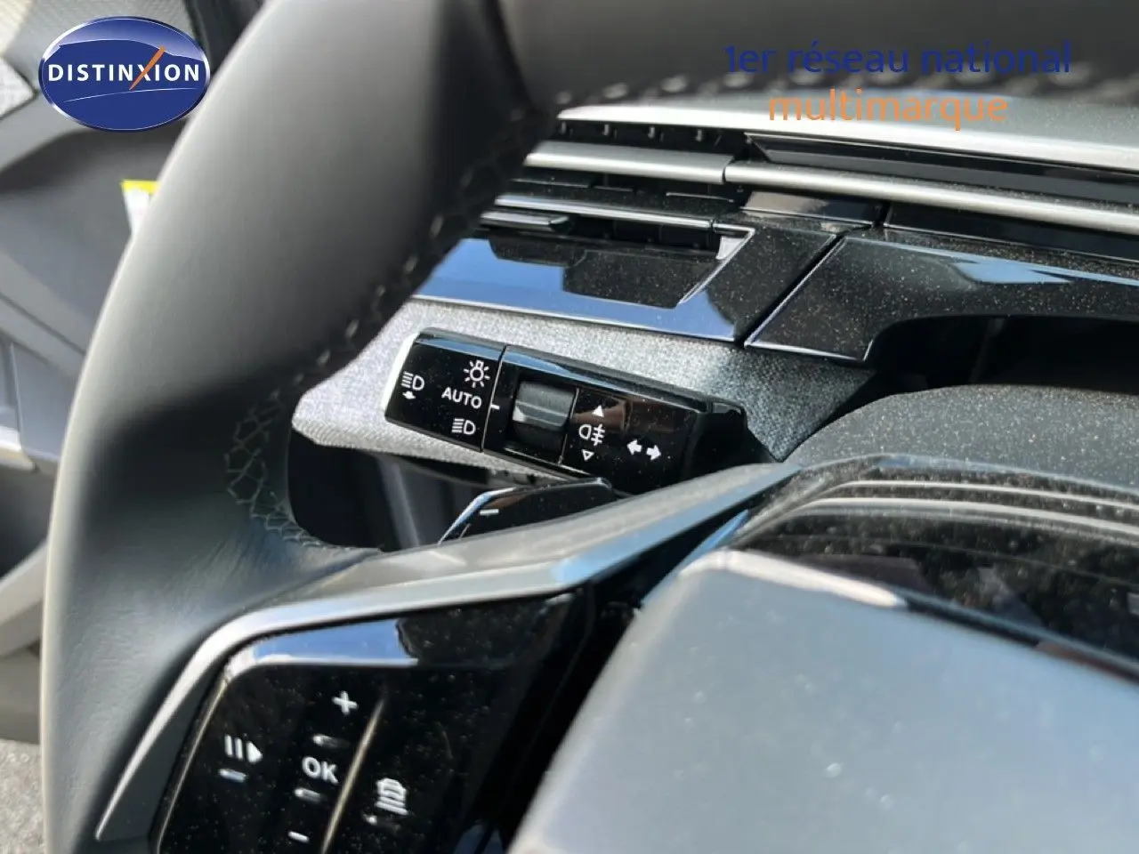 Gros plan sur le volant et la commande des phares du Peugeot 5008 1.2 Hybrid 145ch finition Allure, intérieur noir.
