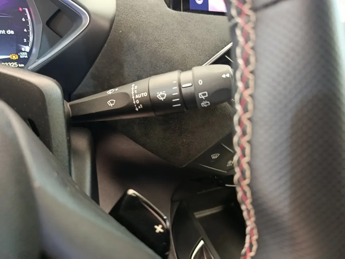 Gros plan sur la manette d’essuie-glace à gauche du volant cuir noir avec surpiqûres rouges dans un DS3 gris foncé 2024.