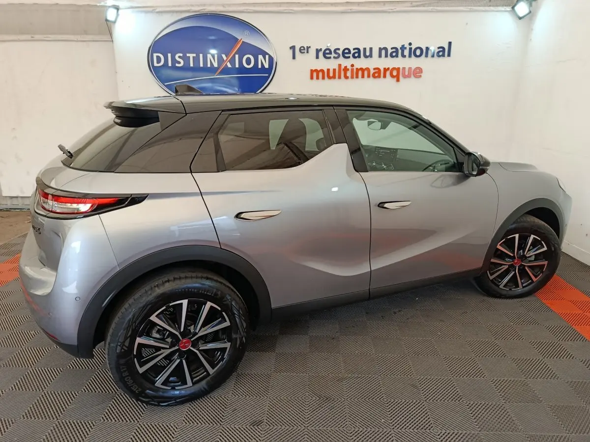 Vue latérale droite d'une DS3 2024 gris foncé avec jantes noires et toit noir, stationnée en intérieur sur sol damier.