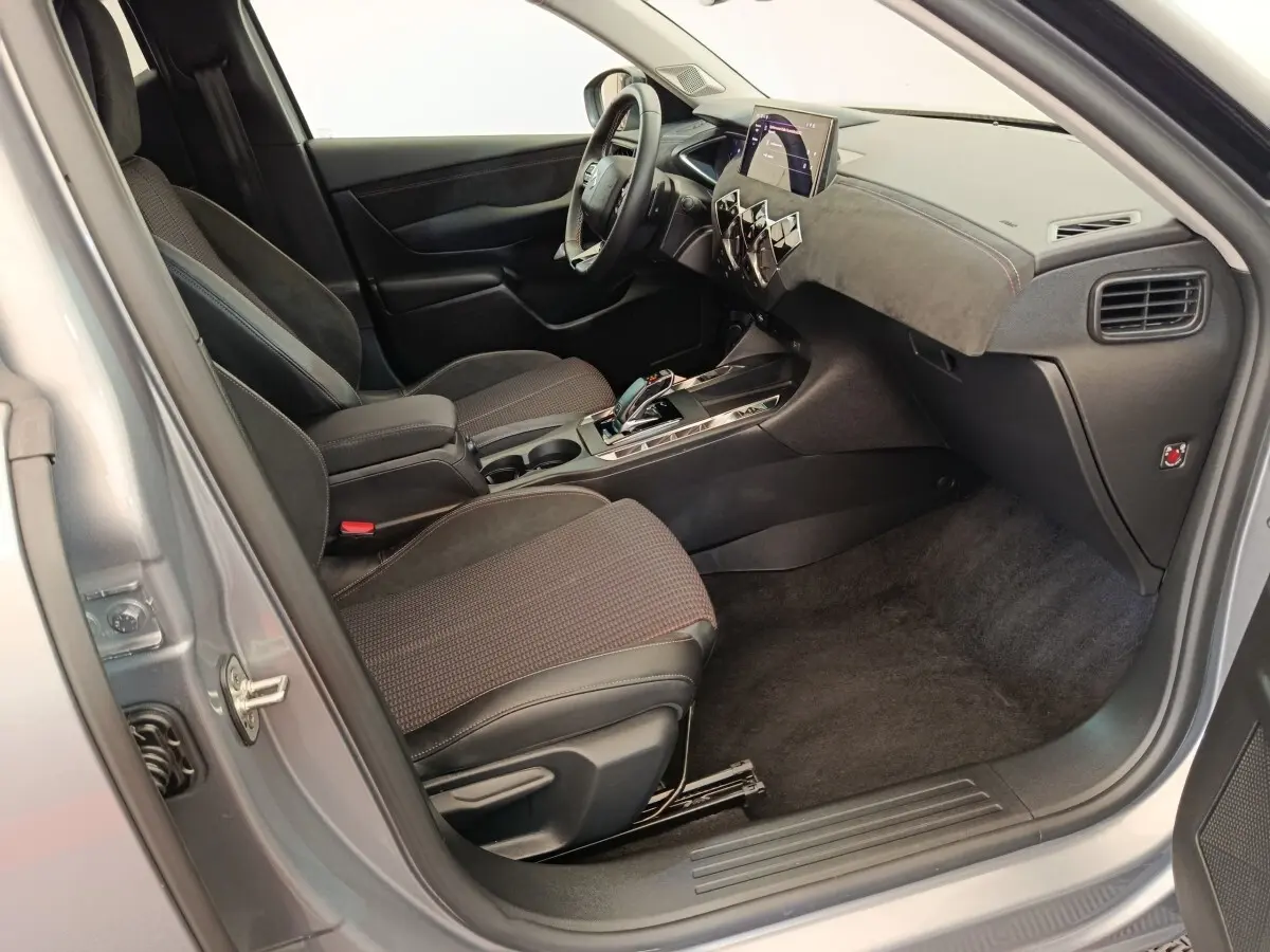 Vue intérieure côté passager d'une DS3 2024 gris foncé, avec tableau de bord moderne et sièges tissu noir.
