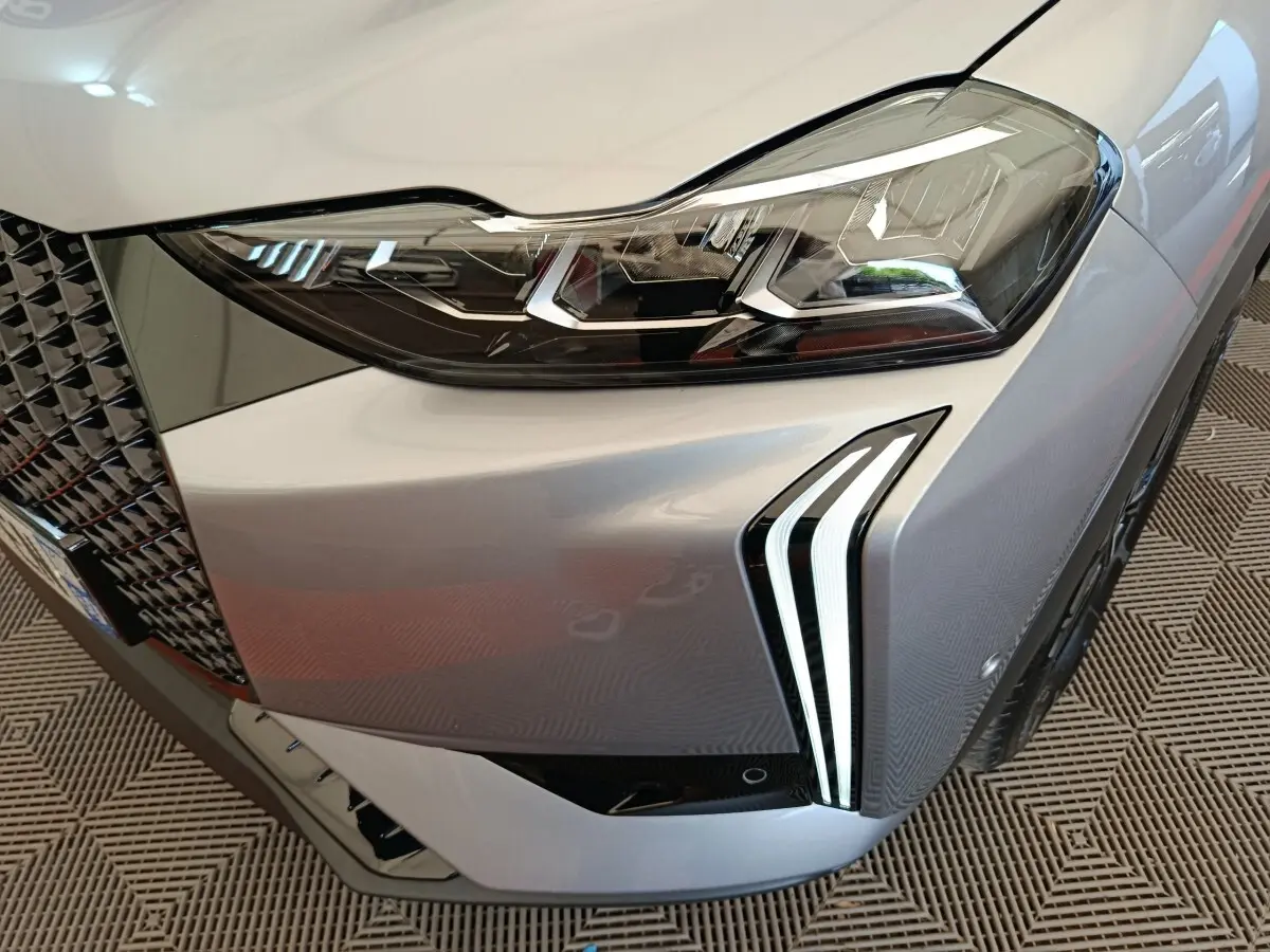 Gros plan sur le phare avant droit gris foncé du DS3 2024 avec signature lumineuse LED distinctive et calandre texturée.