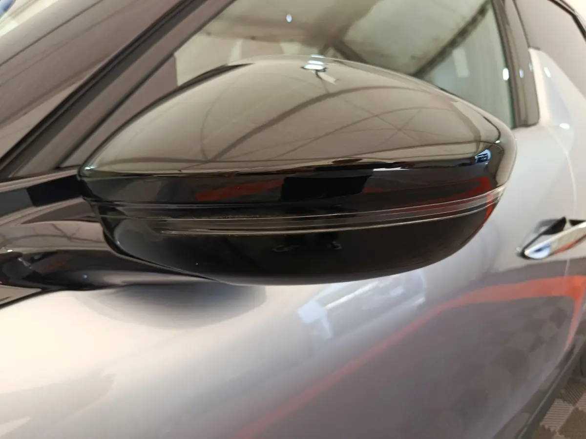 Gros plan sur le rétroviseur noir brillant côté gauche d'une DS3 gris foncé, avec reflet de l'environnement intérieur.
