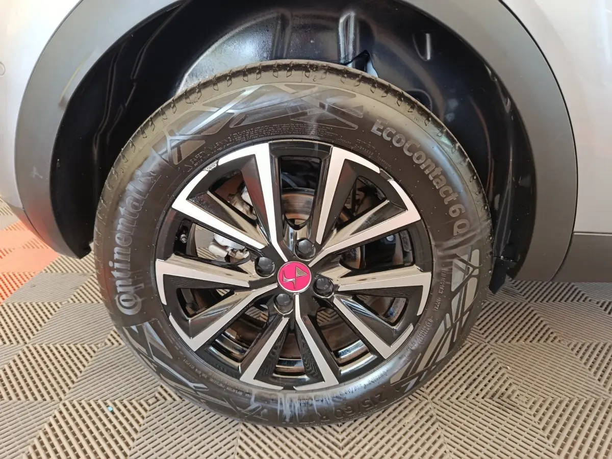 Gros plan sur la roue avant droite du DS3 2024 gris foncé avec jante alliage noire et argentée au logo rose.