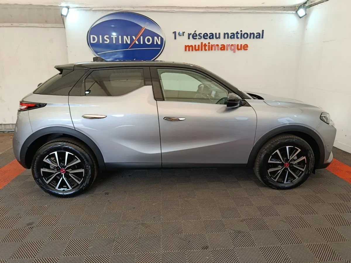 Vue latérale droite d'un DS3 2024 gris foncé avec toit noir et jantes alliage noires, en intérieur showroom.