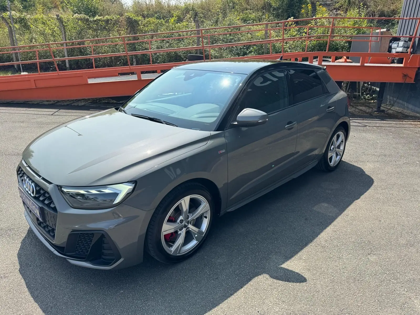 Audi A1 Sportback gris en 3/4 avant droit, avec jantes alliage et étriers de frein rouges visibles.