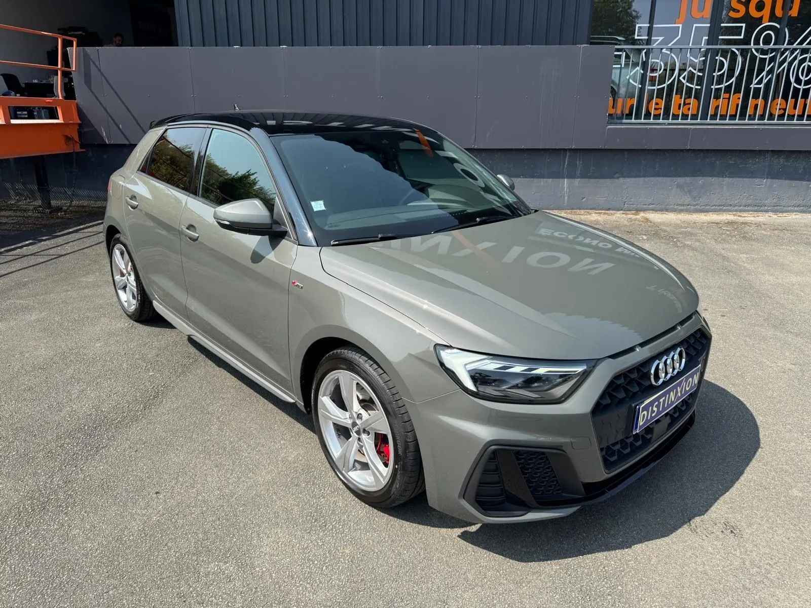 Audi A1 Sportback gris en 3/4 avant droit, avec toit noir et jantes alliage sport S-Line visibles.