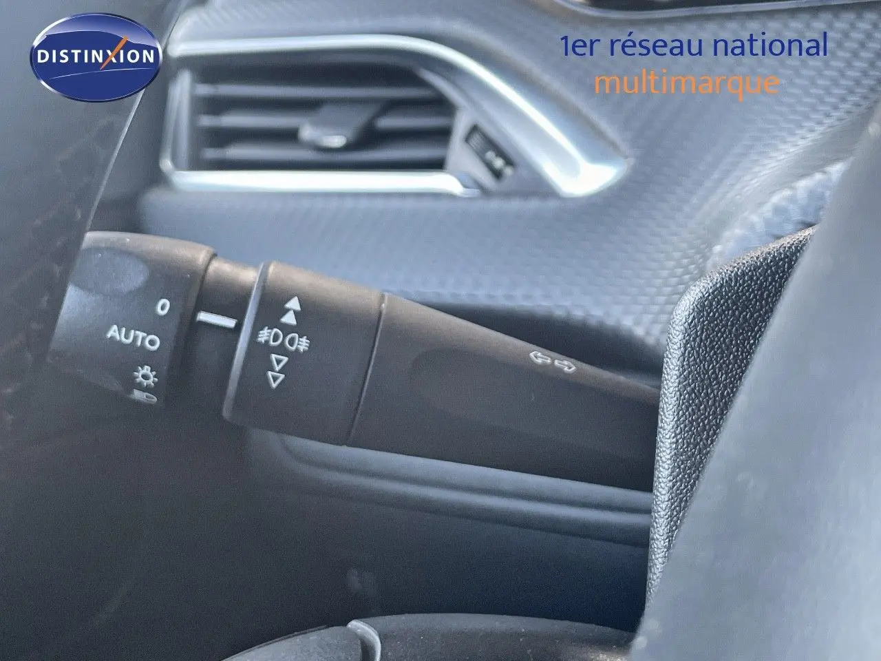 Détail intérieur du commodo d'éclairage à gauche sur Peugeot 2008 gris platinium métal, avec texture de porte visible.