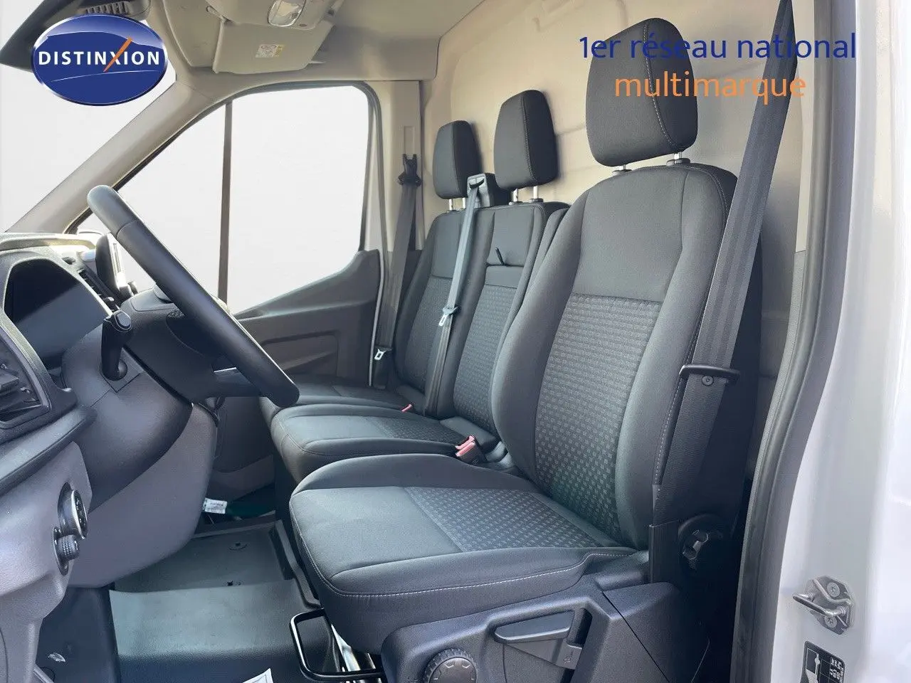Vue intérieure côté conducteur du Ford Transit Fourgon blanc 2023, montrant les sièges avant en tissu noir et le volant.