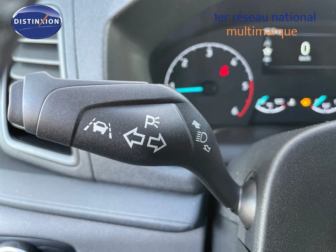 Gros plan sur la manette de clignotant du Ford Transit Fourgon blanc 2023, avec tableau de bord en arrière-plan flou.