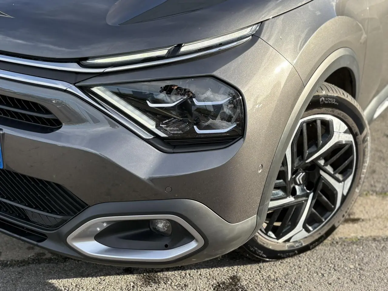 Gros plan sur l'avant droit gris Platinium de la Citroën C4 2024, mettant en valeur le phare LED et la jante alliage 18 pouces.