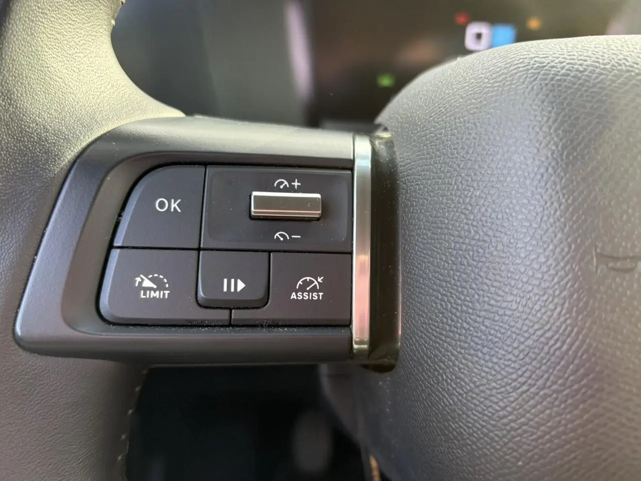 Gros plan sur les commandes noires au volant gris d'une Citroën C4 2024, avec boutons de régulateur et assistant de conduite.