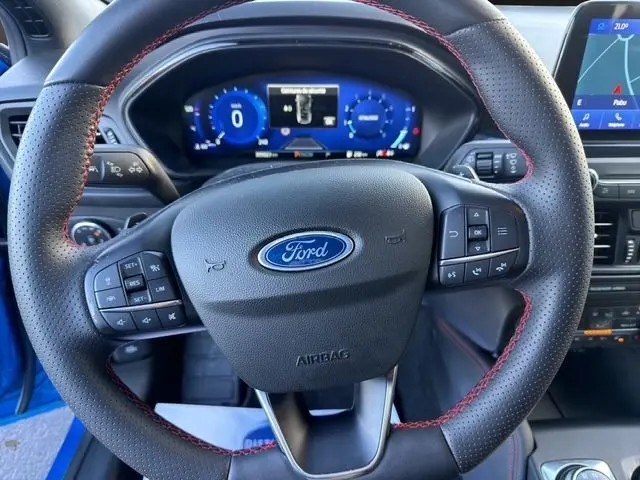 Vue rapprochée du volant en cuir noir avec surpiqûres rouges de la Ford Focus 1.5 EcoBoost 150ch ST-Line 2022, tableau de bord numérique visible.