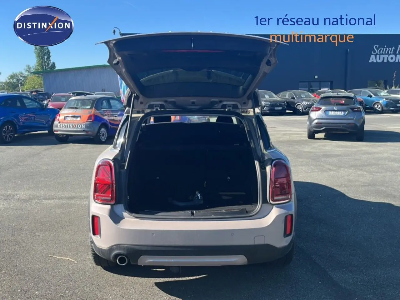 Vue arrière d'une MINI Countryman Cooper grise avec coffre ouvert sur un parking ensoleillé.