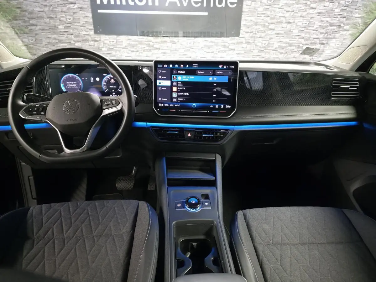 Vue intérieure avant du Volkswagen Tiguan 2025 noir, tableau de bord numérique avec éclairage d'ambiance bleu.