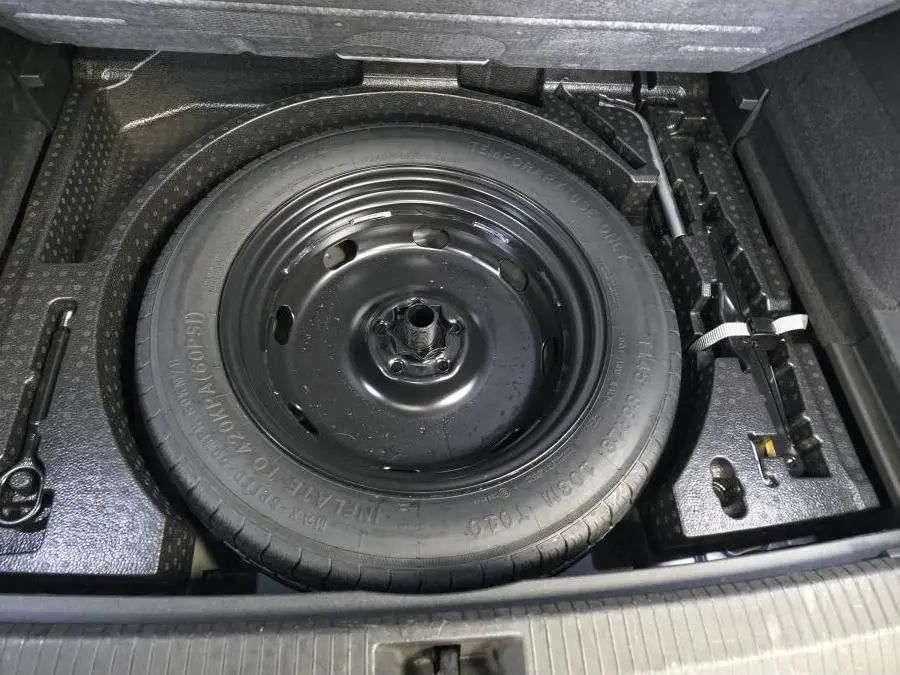 Vue rapprochée de la roue de secours compacte noire dans le coffre du Volkswagen Tiguan 2025 noir.