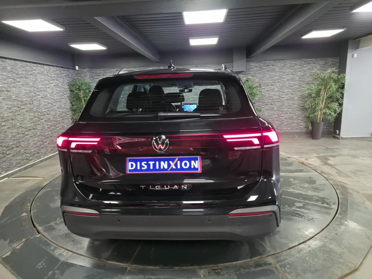 Vue arrière d'un Volkswagen Tiguan noir 2025 avec feux arrière LED allumés dans un showroom.