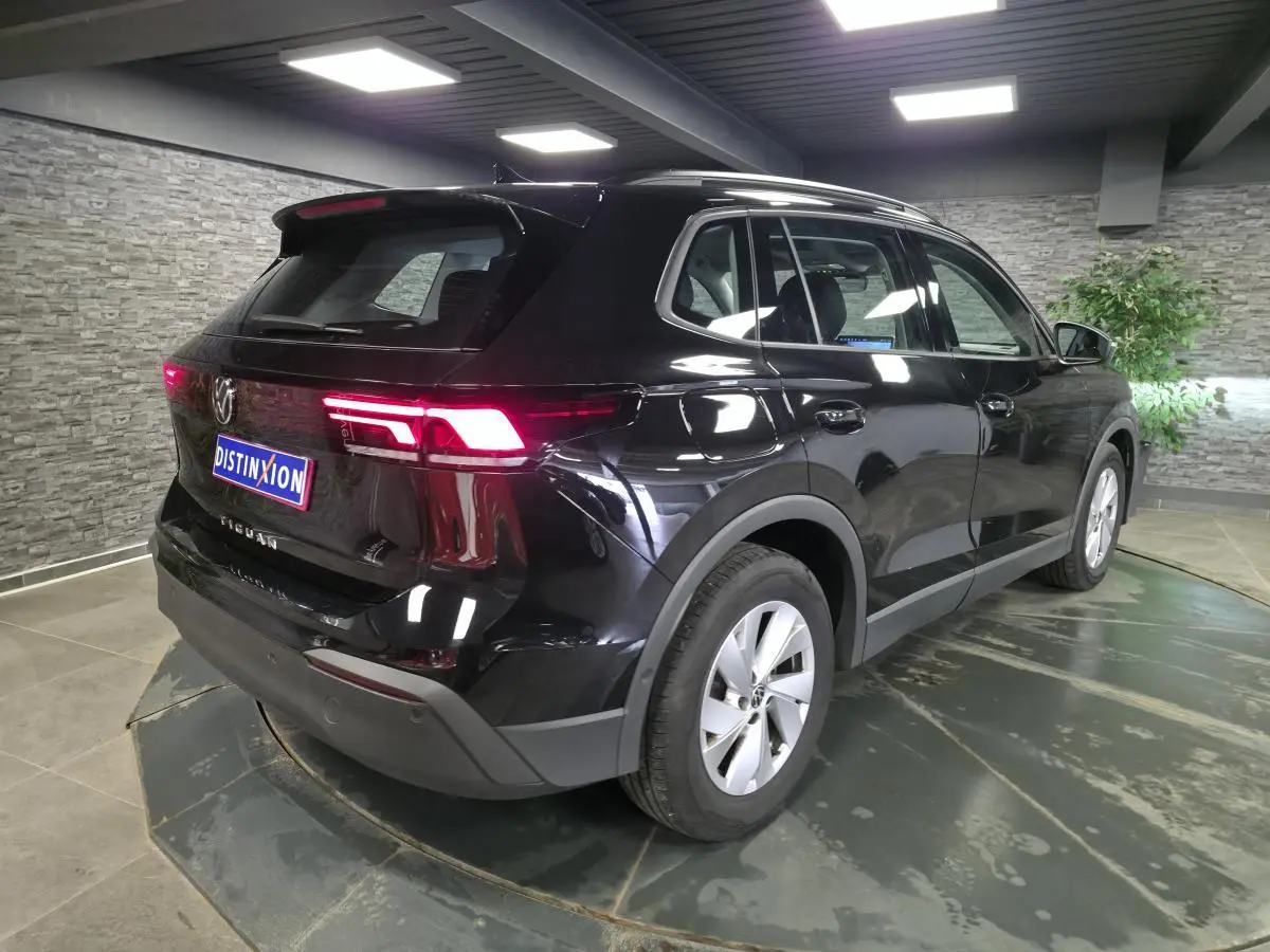Volkswagen Tiguan noir métallisé vu en 3/4 arrière droit, avec feux arrière LED allumés et jantes alliage 17 pouces.