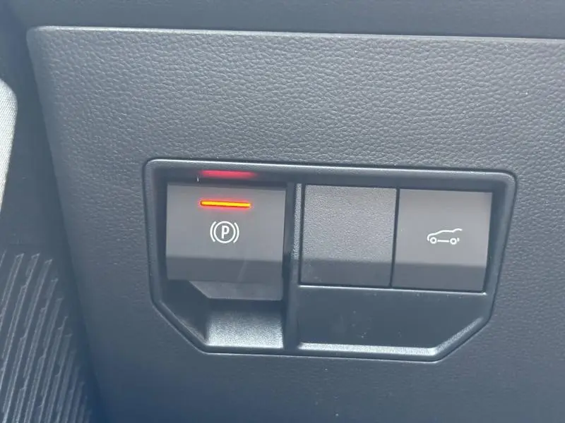 Gros plan sur les commandes de frein à main électronique et ouverture du coffre dans l'habitacle du Dacia Bigster blanc.