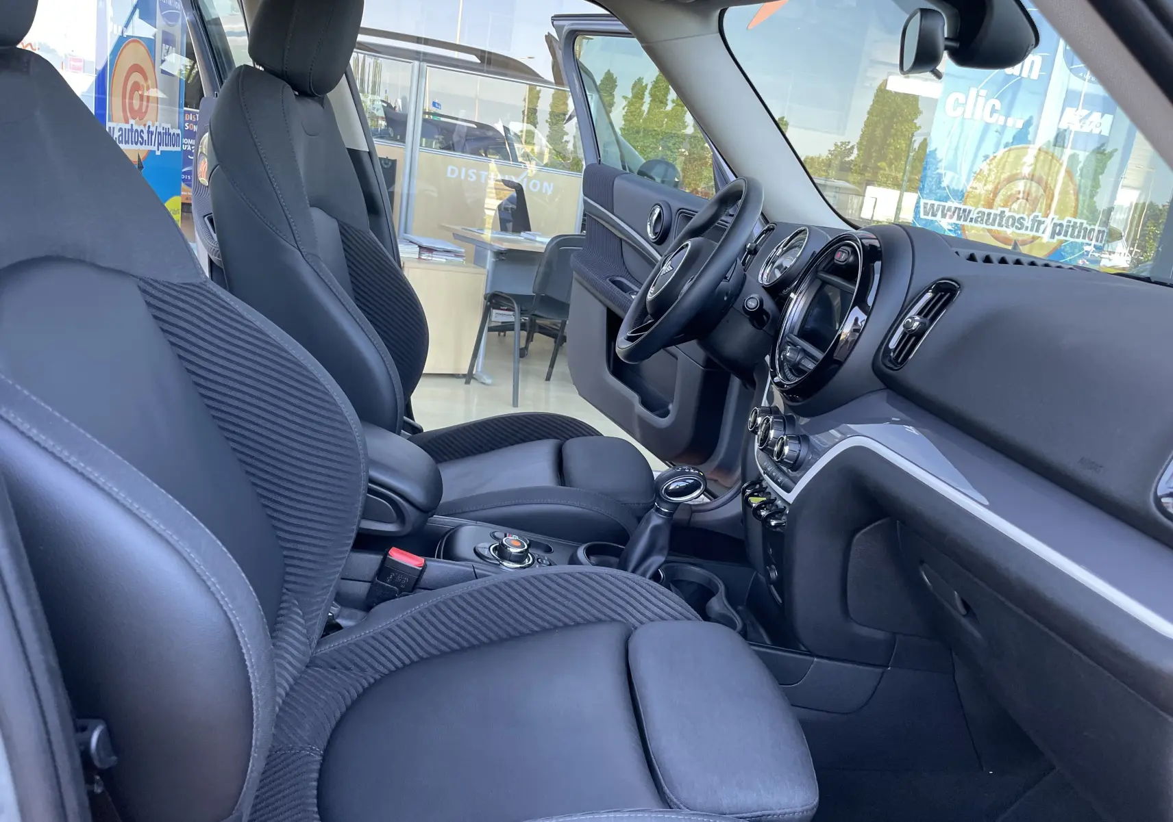 Intérieur avant droit du MINI Countryman F60 hybride, sièges gris noir et tableau de bord moderne avec écran central rond.