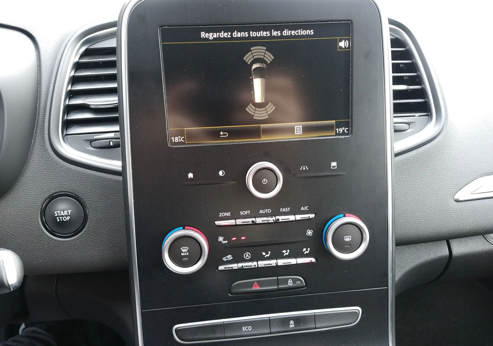 Tableau de bord du Renault Grand Scenic IV 2018 avec écran central affichant l'alerte de proximité et commandes de climatisation visibles.