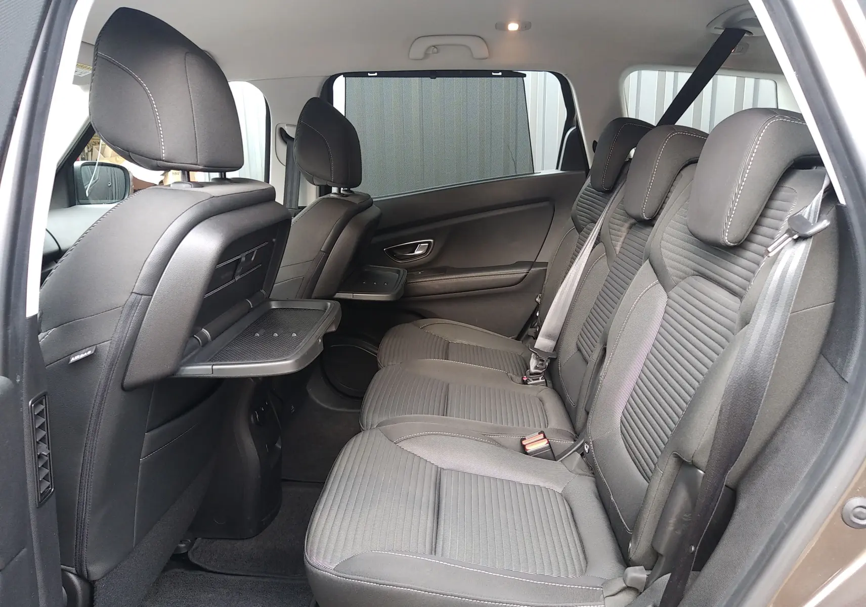 Vue intérieure côté droit des sièges arrière en tissu gris du Renault Grand Scenic IV, avec tablette rabattable sur le dossier avant.