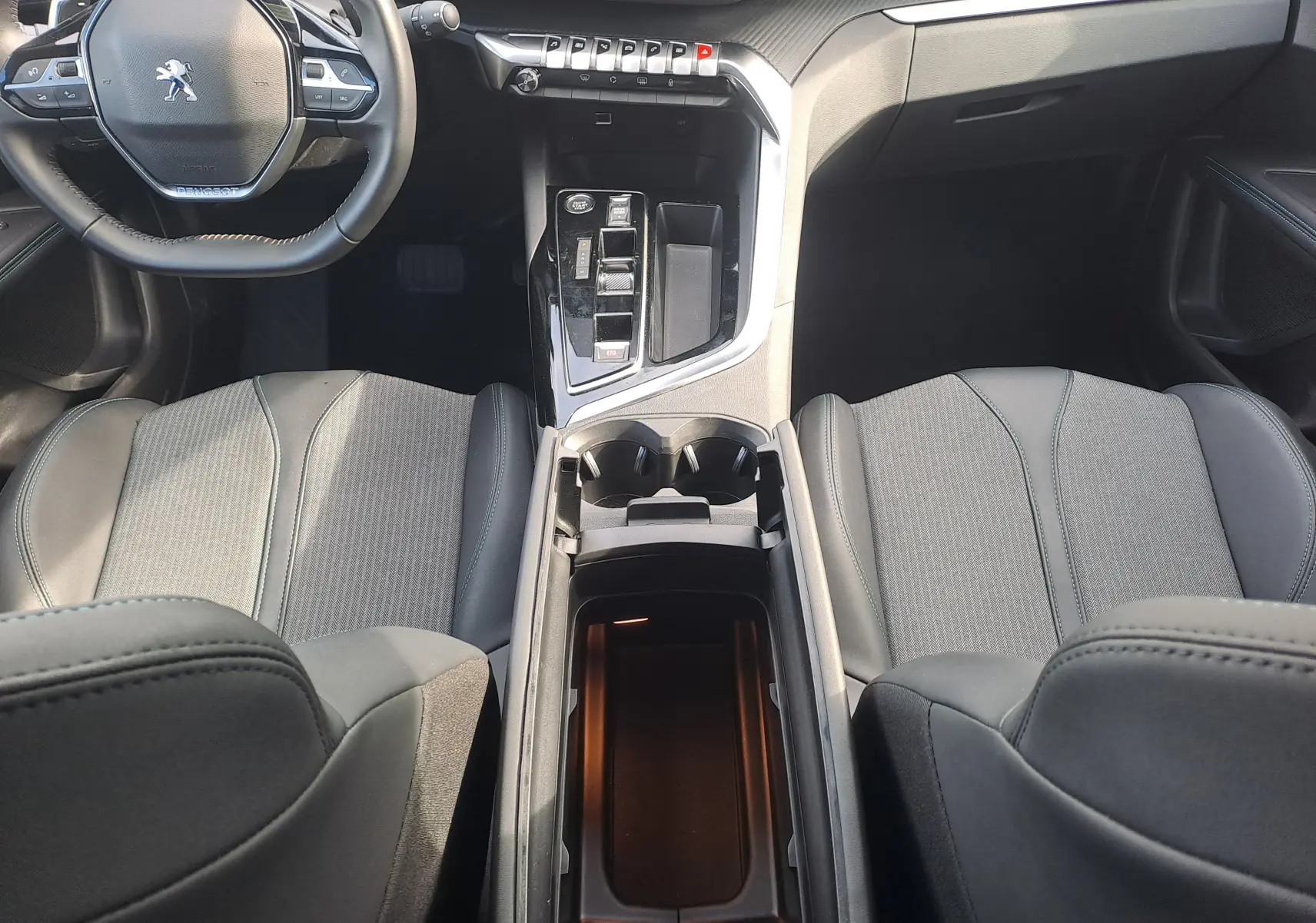 Intérieur du Peugeot 3008 Hybrid 145 en gris, vue plongeante sur sièges, console centrale et volant compact multifonction.