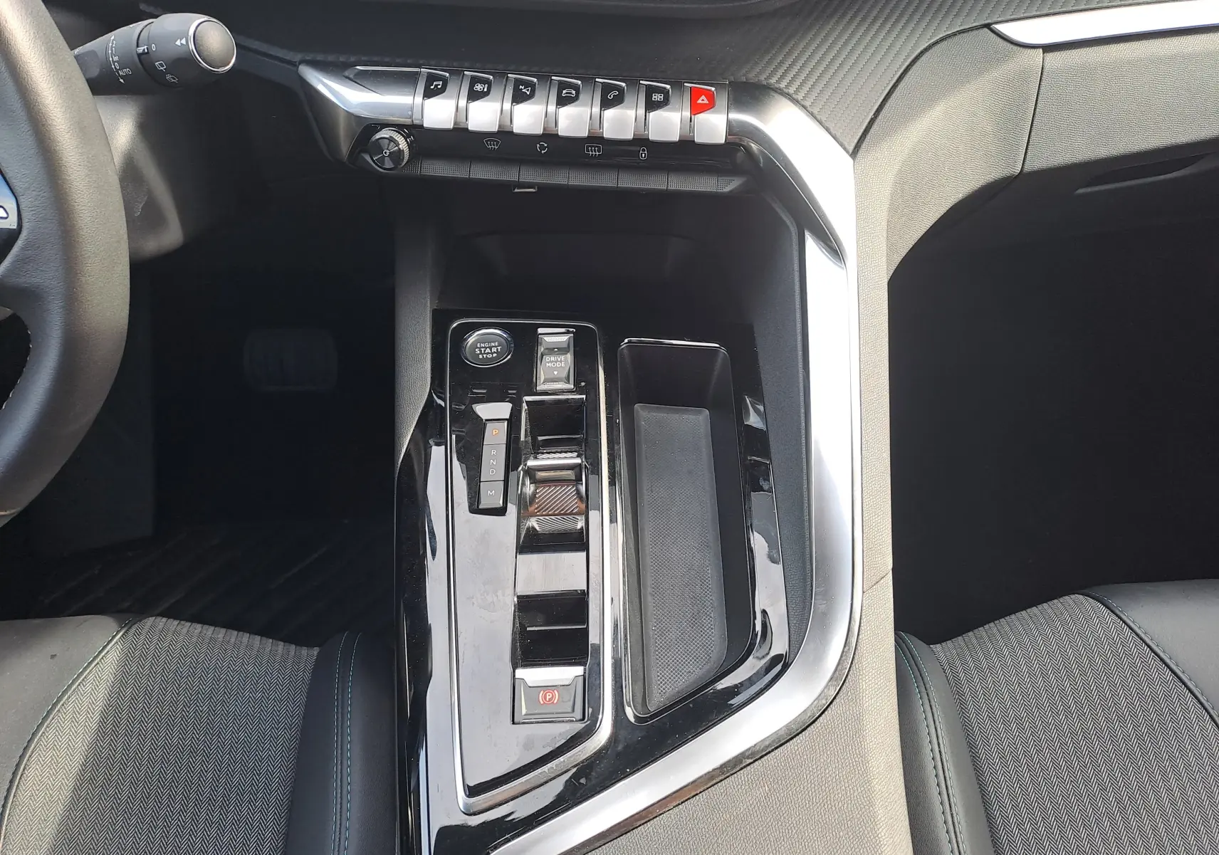 Vue rapprochée de la console centrale noire brillante du Peugeot 3008 Hybrid 145, avec commandes de boîte auto et start/stop.