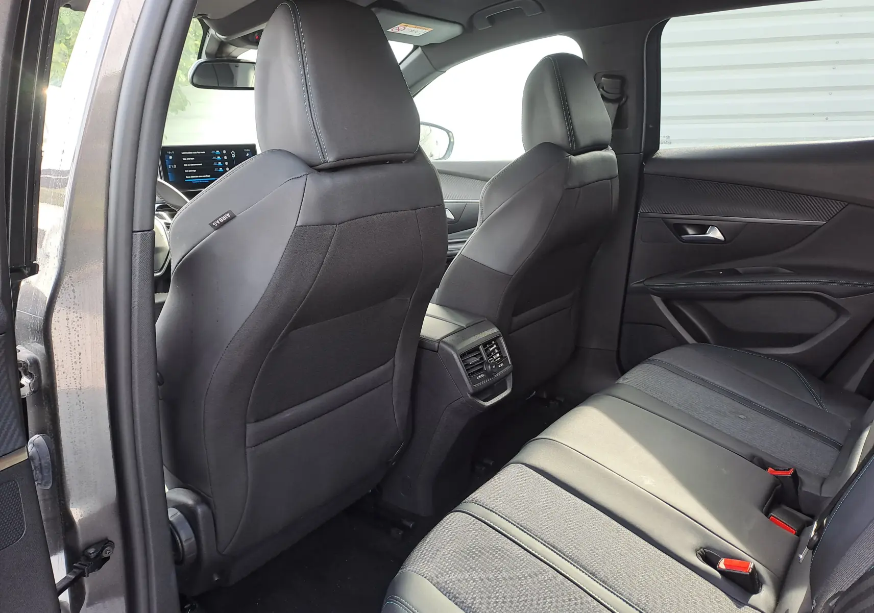 Vue intérieure arrière du Peugeot 3008 Hybrid gris platinium, montrant les sièges noirs et la console centrale avec aérateurs.