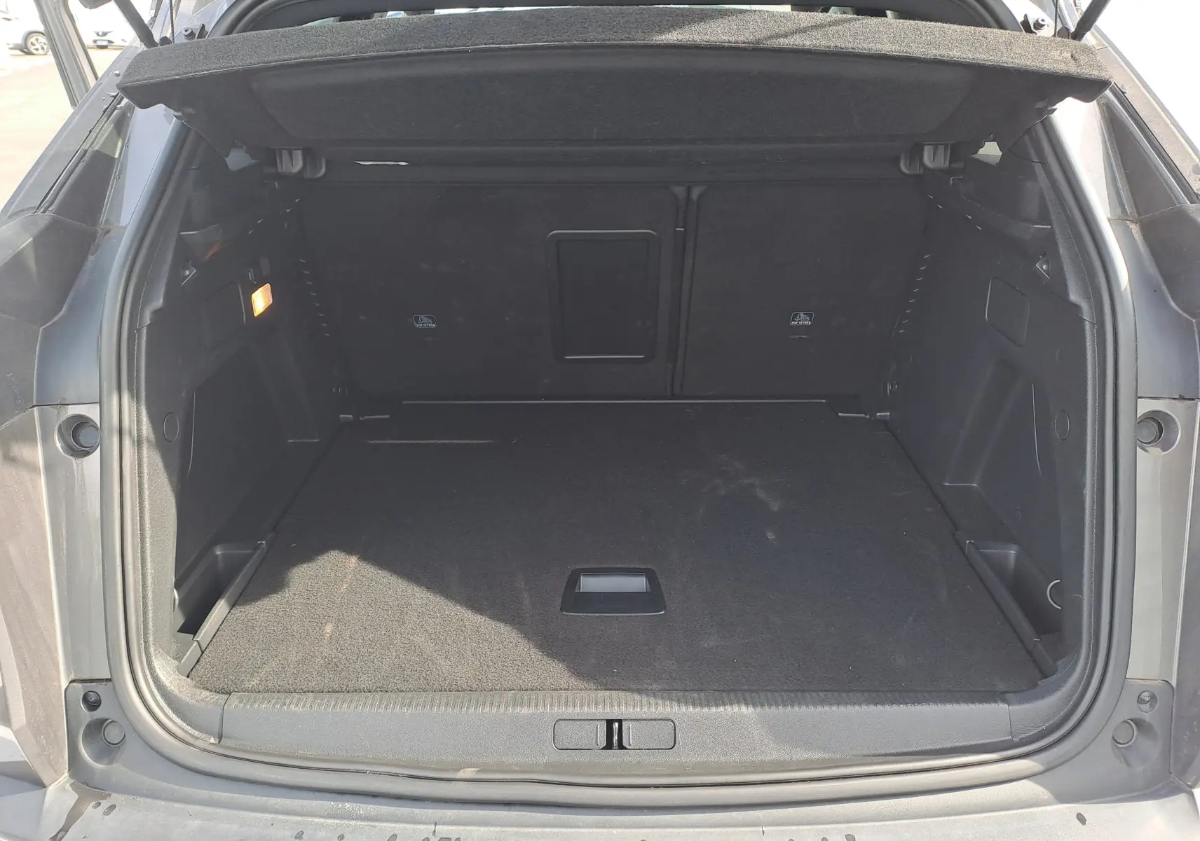 Coffre ouvert d'un Peugeot 3008 Hybrid gris platinium, vue arrière montrant l'espace de chargement vide et la moquette noire.