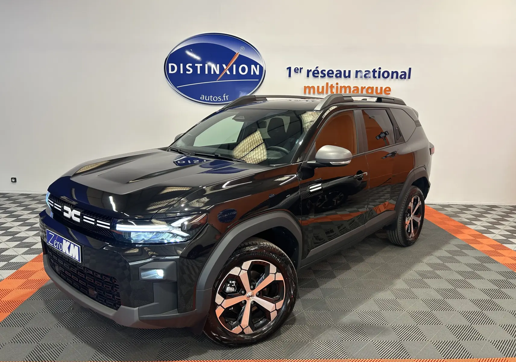 Dacia Bigster 2026 noir nacré en 3/4 avant droit, avec jantes bicolores et hayon électrique visible en arrière-plan.