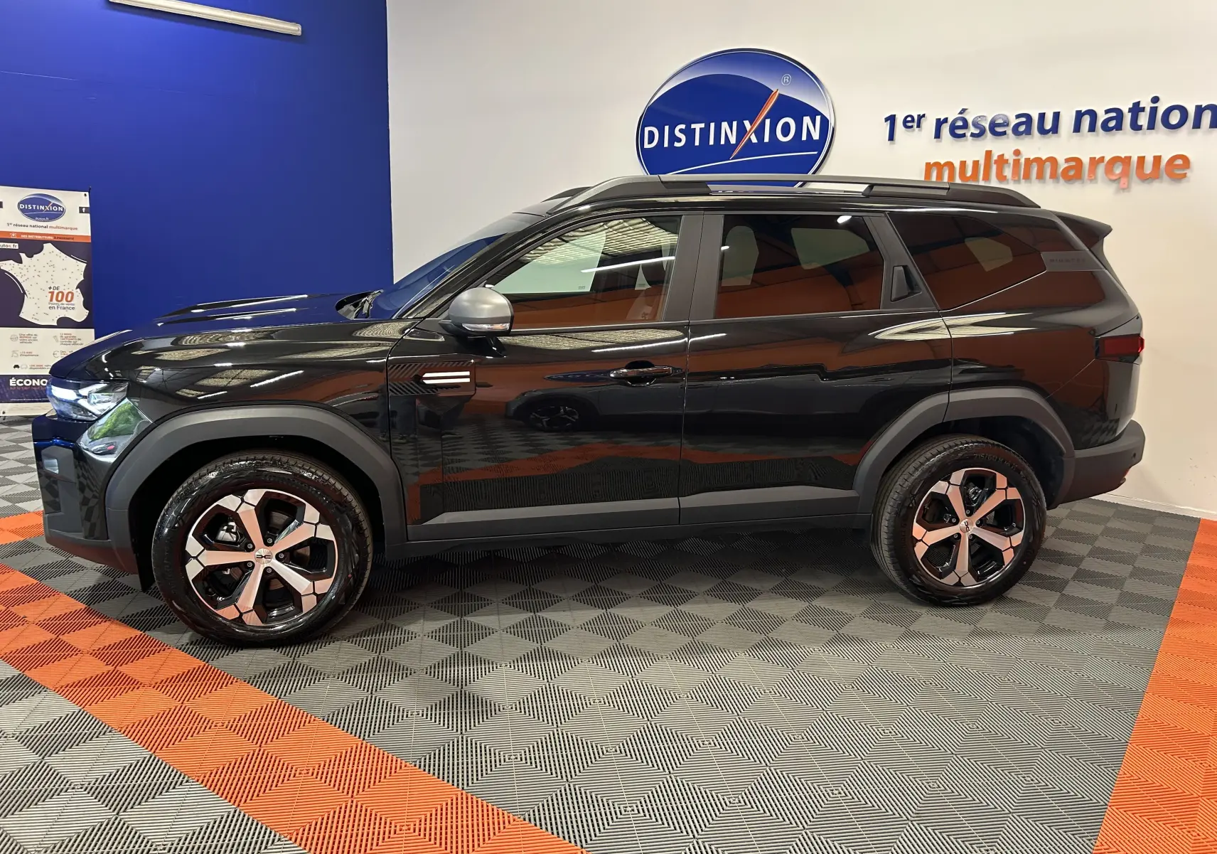 Vue latérale droite du SUV Dacia Bigster noir nacré avec jantes bicolores et toit ouvrant en intérieur showroom.