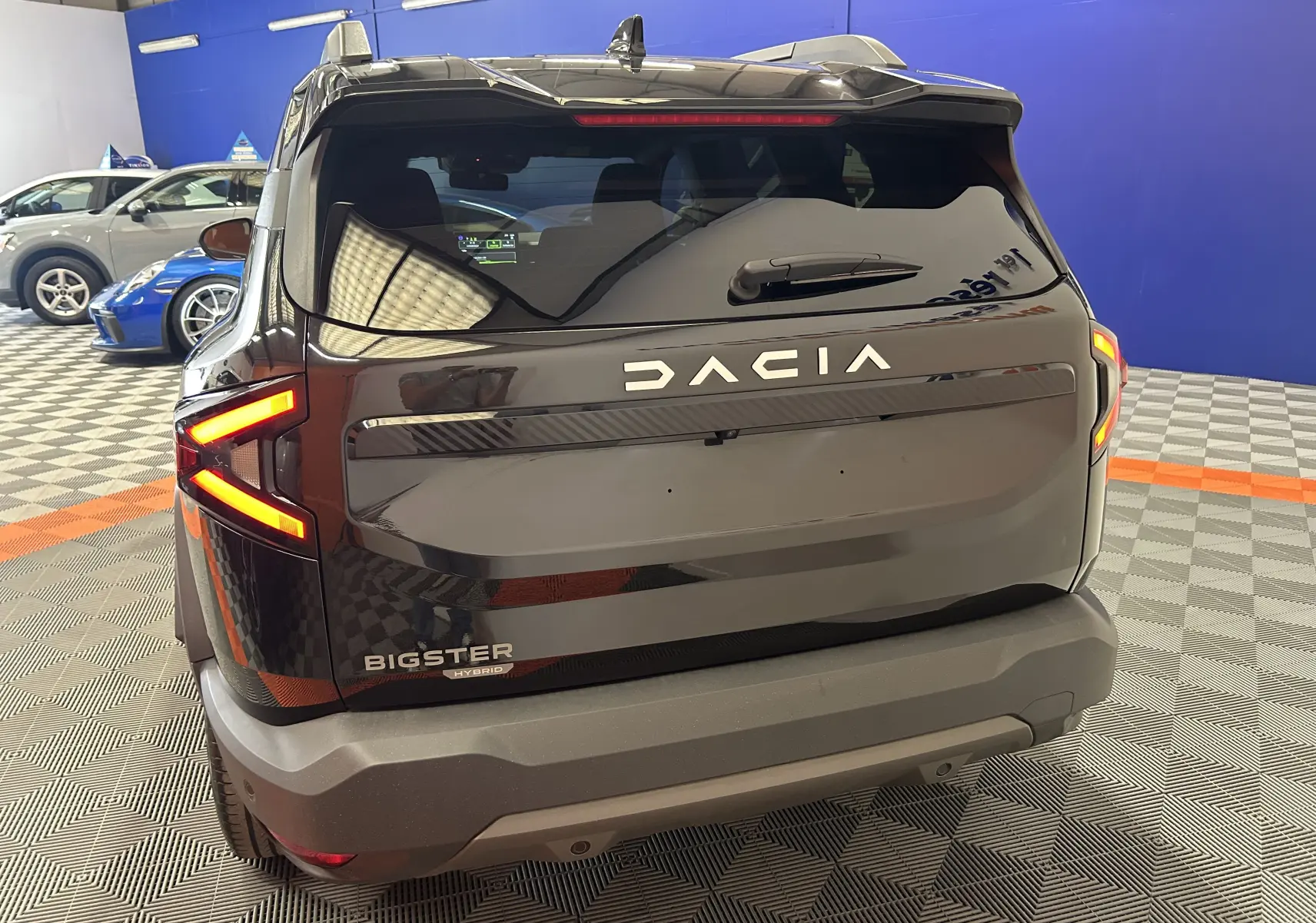 Vue arrière d’un Dacia Bigster noir nacré avec feux LED en forme de flèche et hayon électrique visible en intérieur showroom.