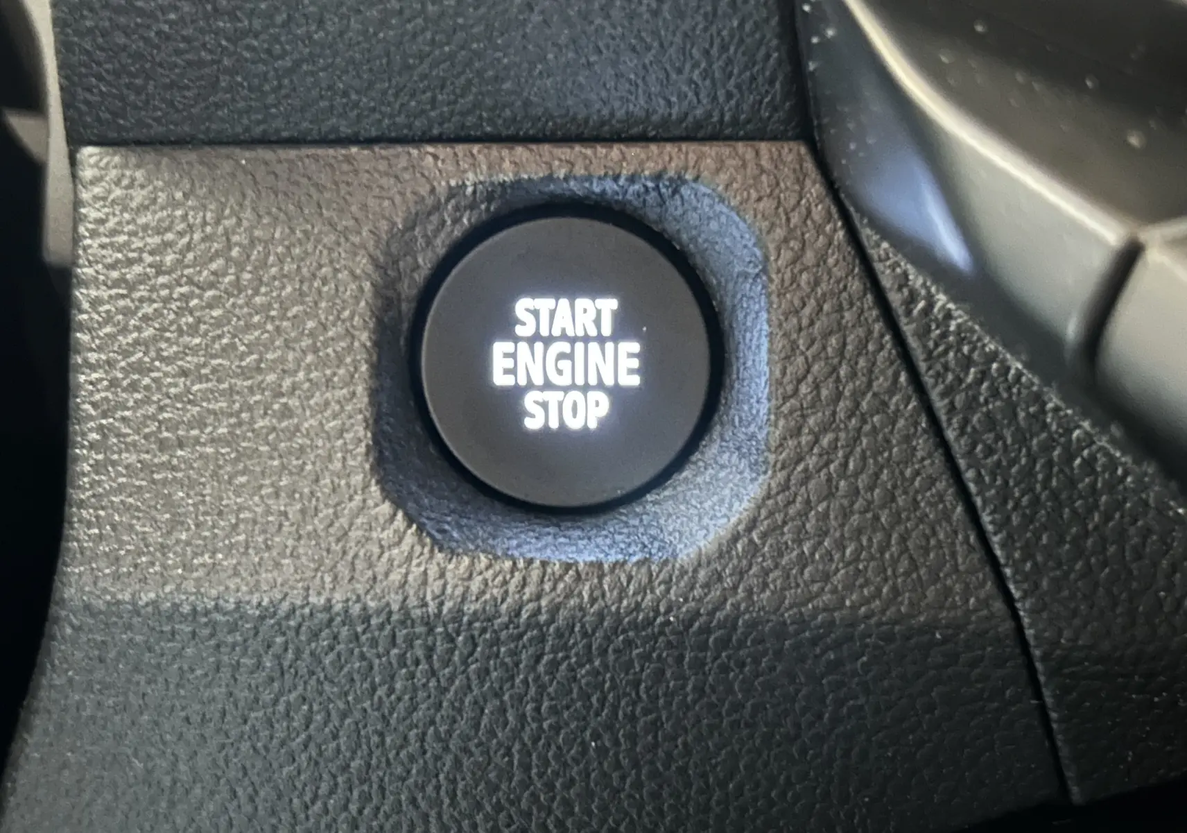 Bouton de démarrage moteur noir avec inscription blanche "START ENGINE STOP" sur tableau de bord texturé.