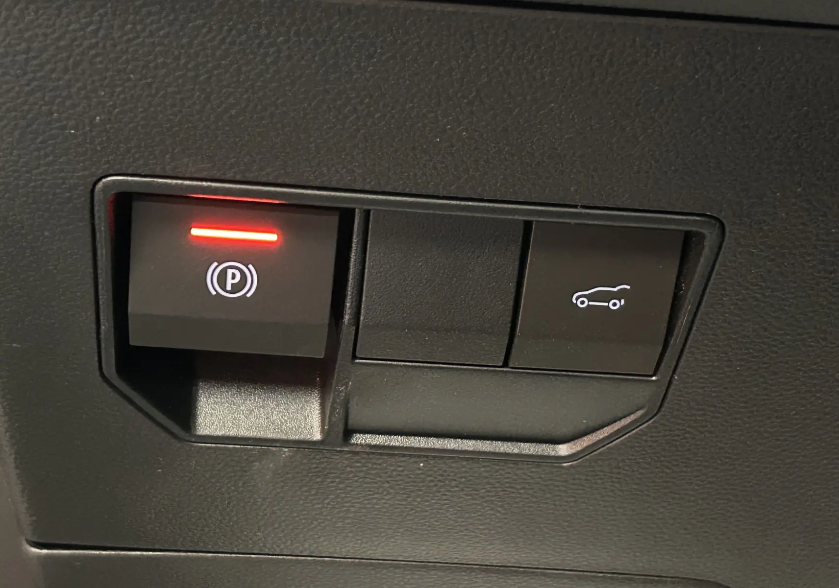 Gros plan sur les boutons de commande du frein à main électrique et du hayon électrique dans l’habitacle du Dacia Bigster noir nacré.