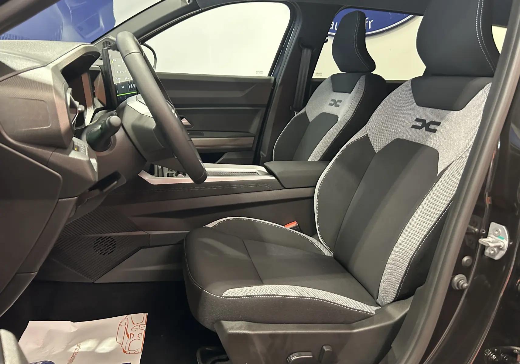 Vue intérieure côté conducteur du Dacia Bigster noir nacré, mettant en valeur les sièges tissu bi-ton avec logo distinctif brodé.
