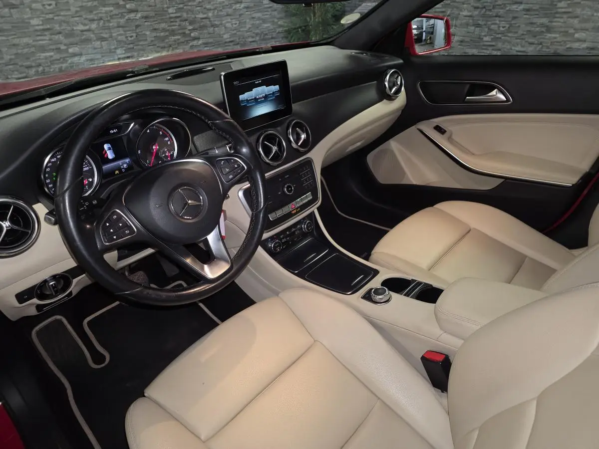 Vue intérieure côté conducteur d'une Mercedes GLA 200 d rouge, sièges en similicuir clair et tableau de bord noir.
