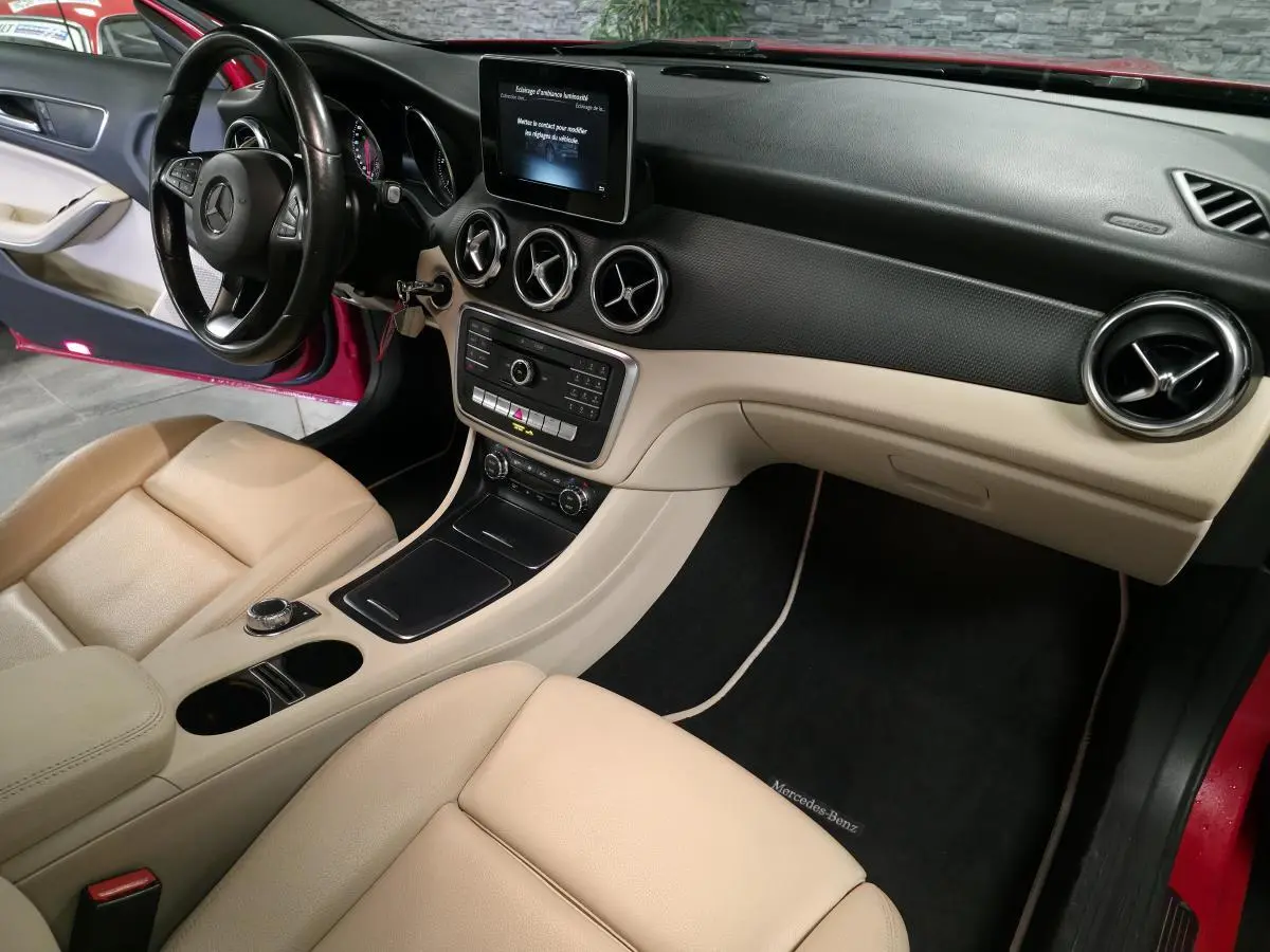 Vue intérieure côté conducteur d'une Mercedes GLA 200 d rouge, avec sièges beige et tableau de bord bicolore noir et beige.