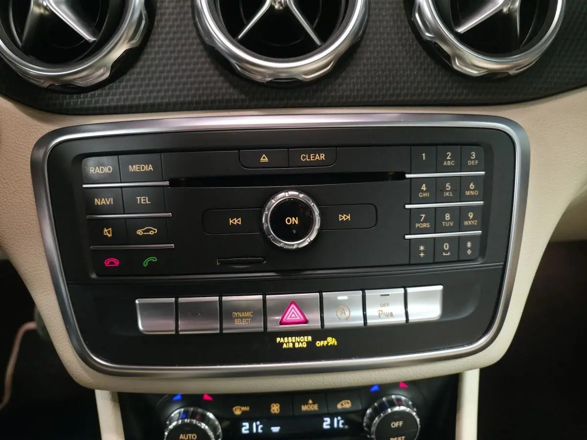 Vue rapprochée de la console centrale beige du Mercedes GLA 200 d rouge, avec commandes multimédia et climatisation.