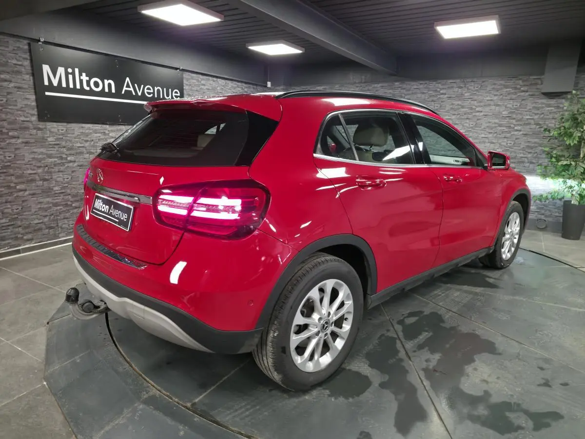 Vue 3/4 arrière droite d'un Mercedes GLA rouge avec attelage rabattable et jantes alliage 17 pouces en showroom.