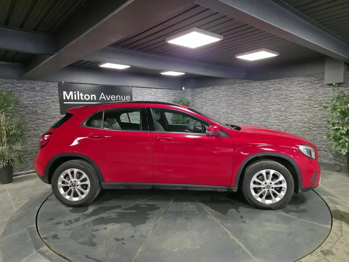 Vue de profil côté gauche d'un Mercedes GLA 200 d rouge avec jantes alliage 17 pouces dans un showroom.