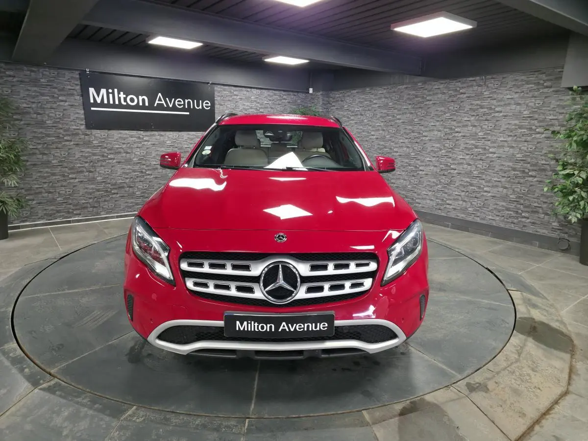 Vue avant d'un Mercedes GLA 200 d rouge brillant avec calandre chromée et logo étoile au centre, en showroom.